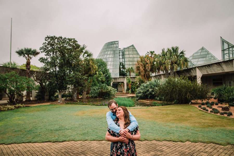 Creative natural and colorful Engagement session at San Antonio Botanical garden. Couple wearing jeans and floral dress with pink and blue tones.